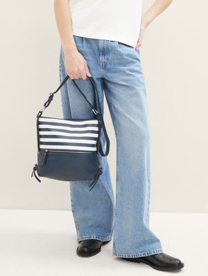 Personne portant un jean large bleu clair et des chaussures noires tient un sac à main bleu marine et blanc à rayures avec une bandoulière.