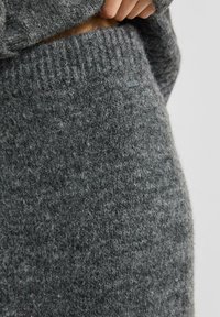 Gestrickter grauer Pullover mit dickem Rippkragen und -saum. Das weiche, strukturierte Material hat ein kleines Logoetikett in der Nähe der Taille.