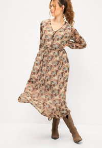 Langes, blumiges Kleid mit V-Ausschnitt, Knopfdetails und Gürtel in der Taille. Hergestellt aus leichtem Stoff in sanften, erdigen Tönen und fließendem Saum.