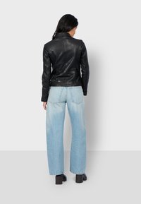 Black leather jacket with a fitted design, paired with light blue high-waisted wide-leg jeans and black chunky heels.