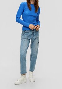 Maglietta a maniche lunghe a coste blu abbinata a jeans larghi di un blu chiaro con tasche frontali e sneakers bianche alte.
