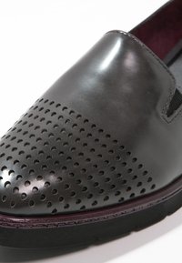Scarpa nera in pelle slip-on con design della punta perforato e accento viola lungo la suola. Texture liscia, profilo basso e soletta imbottita.