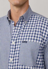 Blau-weiß karierte Button-down-Hemd mit Kragen, Tasche und einem kleinen Logo auf der Tasche. Baumwollstoff mit glatter Textur.