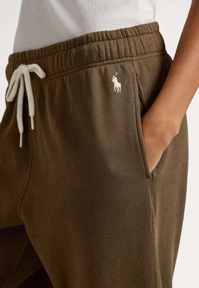 Brune joggebukser med elastisk midje og hvit snor; har sidelommer og en liten brodert logo på øvre venstre lår.