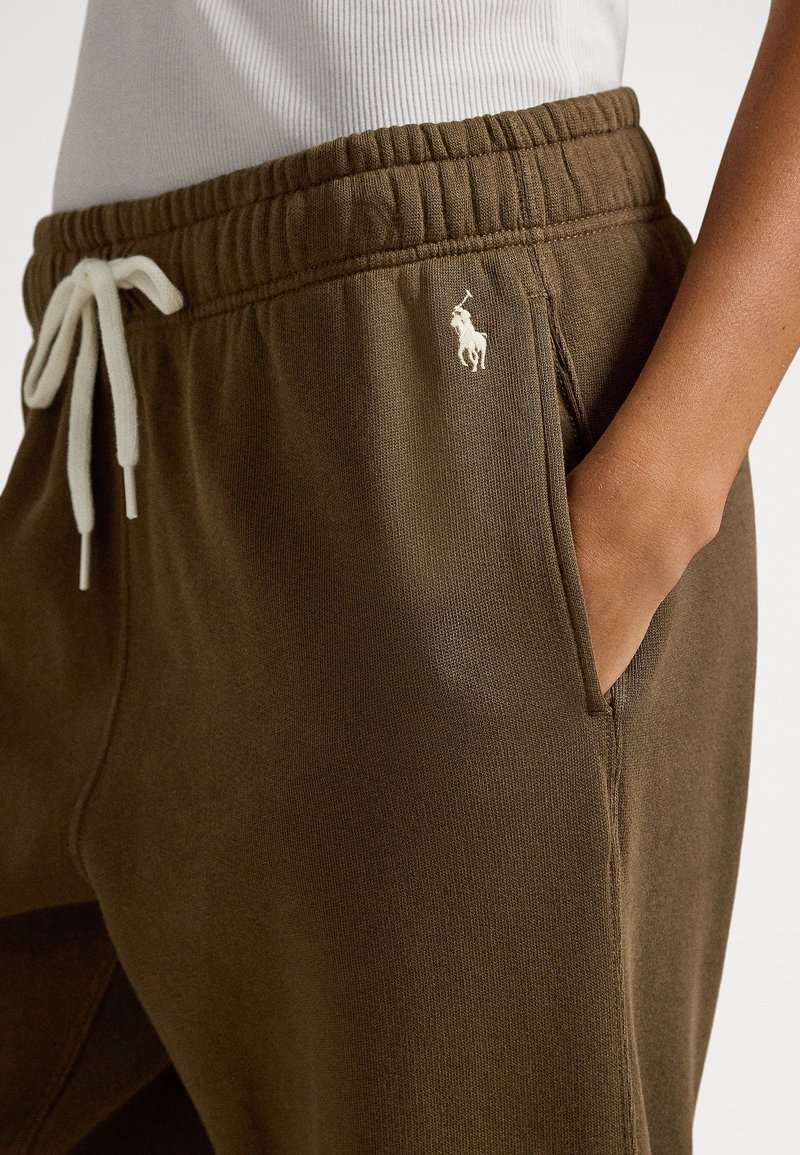 Bruna mjukisbyxor med resår i midjan och vit dragsko; har sidofickor och en liten broderad logotyp på övre vänstra låret.