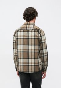 Καρό φανελένιο πουκάμισο σε καφέ και κρεμ αποχρώσεις, με μακριά μανίκια, κουμπωτά μανσέτες και καμπυλωτό τελείωμα, με μαύρες λεπτομέρειες στο σχέδιο.