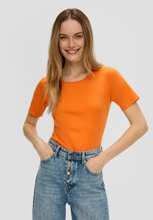 Pomarańczowa koszulka z krótkim rękawem i okrągłym dekoltem, w połączeniu z jasnoniebieskimi dżinsami z wysokim stanem, wyposażonymi w zapięcie na guziki i kieszenie z przodu.