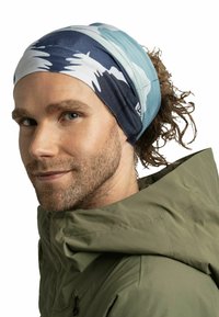 Multicolor headband with a pattern of blue and white waves, made of soft fabric. Worn with a green jacket, showcasing a relaxed design.