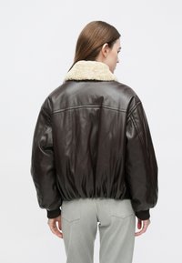 Bruine leren bomberjack met een beige shearlingkraag, elastische manchetten en zoom, met een ontspannen pasvorm en een gladde textuur.