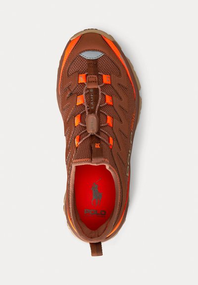 Brauner Sportschuh aus Mesh-Stoff mit orangefarbenen Akzenten, geformter Sohle und elastischen Schnürsenkeln. Das Innere ist mit einem roten Futter und Logodetails versehen.
