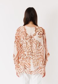Blusa leggera e trasparente di colore crema con motivi a zebra e leopardo marroni; presenta una vestibilità morbida e maniche drappeggiate per una silhouette fluida.
