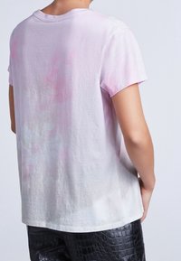 Camiseta de corte relajado en tejido rosa claro, con un estampado de tie-dye en tonos suaves y cuello redondo. Mangas cortas, con un dorso ligeramente más largo.