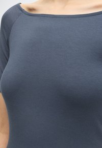 Gros plan d'une personne portant un t-shirt gris foncé ajusté avec un large décolleté découvrant une épaule.