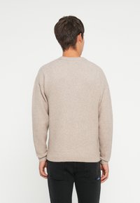 Beige knit sweater with a crew neck, long sleeves, and ribbed cuffs and hem. Soft texture, relaxed fit, plain design, and no visible patterns.