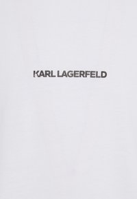 Bílá bavlněná tričko s nápisem "KARL LAGERFELD" černou barvou, vytištěným uprostřed v tučném bezpatkovém písmu. Hladká textura.