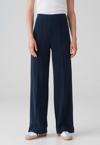 Navy wijde broek met een hoge elastische tailleband, zijplooien en een gladde textuur. Gecombineerd met witte sportschoenen.