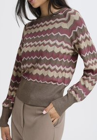 Strickpullover mit Zickzackmuster in Bordeaux, Beige und Rosa, mit einem gerippten braunen Bund und Bündchen, der strukturiertes Material präsentiert.