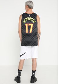 Persoon met kort grijs haar staat met de rug naar de camera, draagt een zwart NBA-jersey met nummer 17 "Schröder" en witte Nike-shorts.