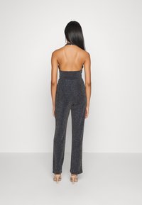 Svart halterneck jumpsuit med glittrande textur, figurnära midja och vida ben. Slätt material med glänsande detaljer vid halsringningen.