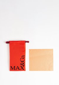 Punainen kangaskassi, jossa on musta "MAX & Co." -logo, yhdessä teksturoituun beigeen neliöön, jossa on kohokuvioituja brändielementtejä.