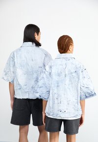 Denimjakke med lyseblå, slitt finish, korte ermer, frynsete kanter og en avslappet passform, kombinert med mørke shorts.
