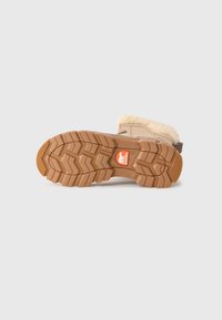 Vinterstøvel liggende på siden som viser tykk, mønstret brun såle med Sorel-logo og beige fôrkantet overdel.