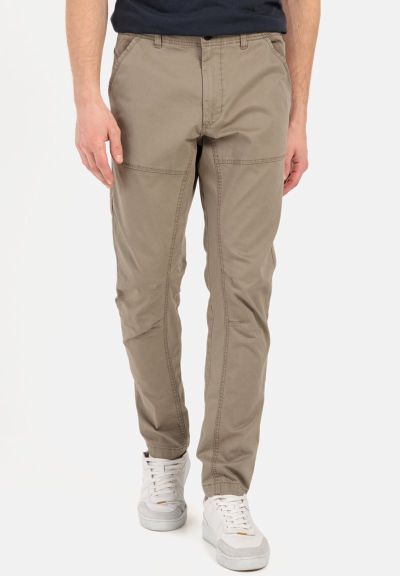Beige katoenen broek met een slim fit, voorzien van platte zakken en gestikte accenten langs de zijkanten. Gepaard met witte sneakers.
