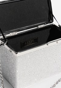 Ezüst színű, doboz alakú kis táska strasszokkal díszítve, fekete belsővel és lánc pánttal. Belsejében LIPSY logó található.