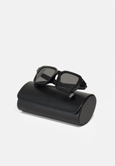 Mustad musta raami ja tumedate läätsedega tumedad prillid, mis puhkavad ümmarguse musta nahkümbriku peal, millel on eespool graveeritud "Giorgio Armani".