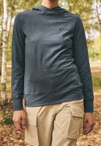 Mörkblå huvtröja med små vita prickar, långa ärmar och en logotyp på bröstet; kombinerad med beige cargobyxor.