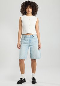 White cropped sweater with button closure, paired with light blue denim shorts, black loafers, and white socks. Plain background.