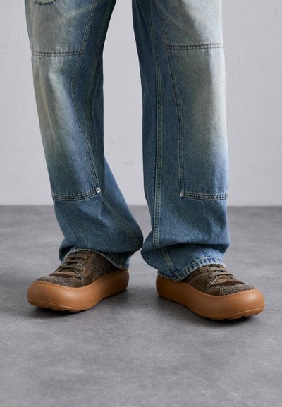 Adidași texturați maro cu o talpă groasă de culoare bej, design cu șireturi și accente gri închis, asortați cu blugi de denim deschis, ușor decolorati.