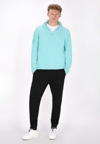 Lichtblauwe fleece pullover met een ritskraag, gecombineerd met zwarte tapered joggers en witte sneakers. Soepele textuur, casual pasvorm.