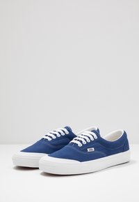 Blaue Canvas-Sneaker mit weißen Gummisohlen und Schnürsenkeln. Verfügt über kontrastierende Nähte und ein kleines Markenlogo an der Seite. Klassisches Low-Top-Design.