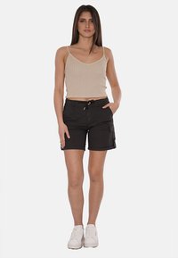 Pantaloni cargo neri con tasche, abbinati a una canotta a coste beige. L'outfit è completato da sneakers bianche.
