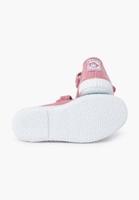 Zapato textil rosa con suela de goma blanca, presenta un diseño plano, correa ajustable y una etiqueta con una ilustración de un personaje en el talón.