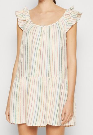 Robe blanche sans manches avec des rayures verticales multicolores et des détails à volants aux épaules portée par une personne aux bras détendus le long du corps.