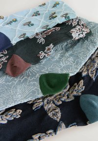 Muestras de tela en varios colores: azul claro, verde oscuro, azul marino y burdeos, con patrones de bordado florales y geométricos.