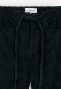 Pantalones de pana negros con una superficie texturizada, que cuentan con una cintura con cordón y dos bolsillos frontales. La etiqueta dice "SCALPERS."