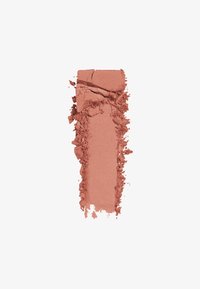 Blush pressato in una tonalità matt, pesca caldo, con texture visibile da un bordo rotto e polvere sciolta sparsa intorno.