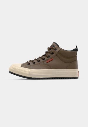Pruun keskmise kõrgusega sneaker, millel on beež kummist varbakate ja tald, mustad detailid ja ümmargused nöörid. Küljel on punane logo silt.