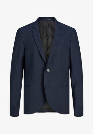 Granatowy garnitur z teksturowanej tkaniny, składający się z jednorzędowej marynarki i spodni w stylu slim fit, zestawiony z białym t-shirtem i białymi trampkami.