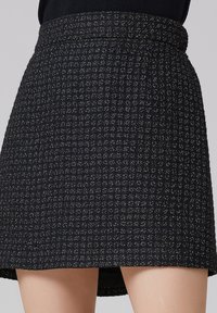 Jupe en tweed noir avec un motif texturé, taille ajustée et un ourlet légèrement évasé, mettant en valeur des touches subtiles de fil métallique.