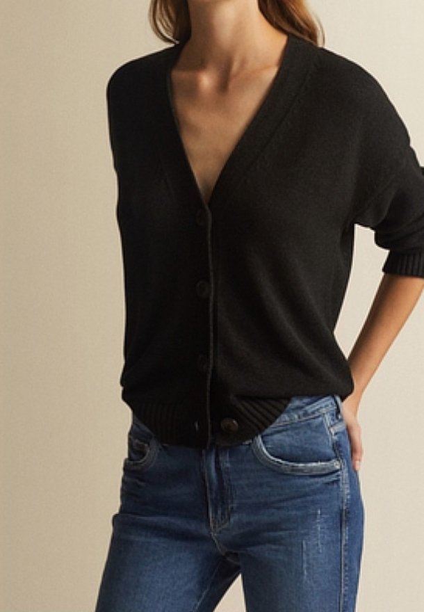 Schwarze Strickjacke mit V-Ausschnitt, Knopfdetails und gerippten Bündchen. Über blauen Jeans getragen, hat sie eine weiche Textur und eine lässige Passform.