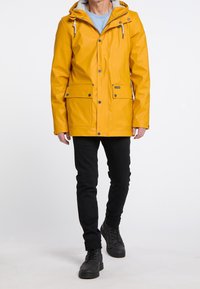 Yellow waterproof jacket with a hood, grey lining, snap buttons, and two front pockets. Worn over black slim-fit pants and black shoes.