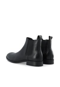 Botas Chelsea de cuero negro con paneles elásticos laterales, punta redondeada y tacón bajo apilado. Textura suave y detalles de diseño minimalista.