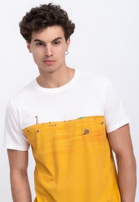 Witte T-shirt met een gele landschapprint van hooibalen en een windmolen, gemaakt van zachte stof met een reguliere pasvorm.