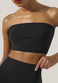 Top bandeau nero con una texture liscia e orlo a coste, progettato per un fit aderente, con la pelle visibile appena sotto il capo.