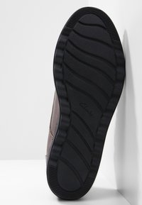 Bruine leren schoen met een zwarte rubberen zool die een golvend profiel heeft en een subtiel merklogo. De hak is laag en afgerond.