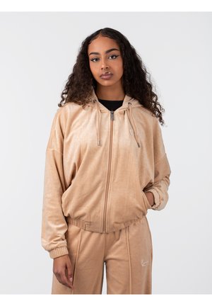 Samtige tanfarbene Bomberjacke mit einem Reißverschluss an der Vorderseite, Kapuze und elastischen Manschetten. Verfügt über ein dezentes Muster und eine Logo-Stickerei auf der Brust.